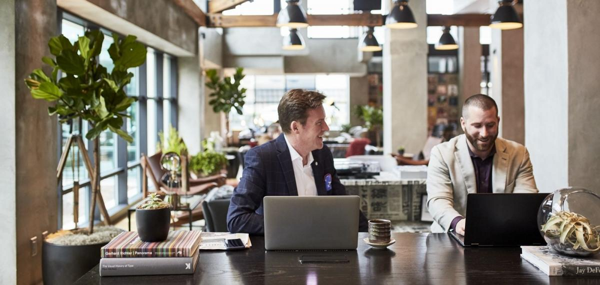 Twee professionals werken met laptops aan een tafel in een lichte kantoorruimte